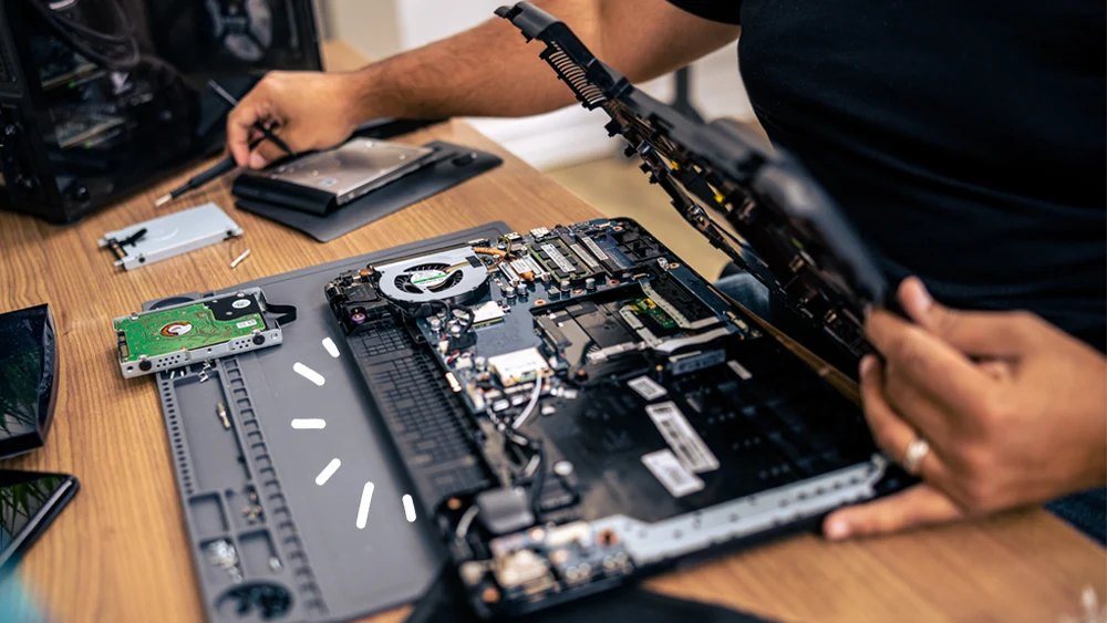 Technician at Zebulun Workshop in Juja carefully soldering a laptop motherboard on a clean workbench, with tools and a laptop chassis open in the foreground.